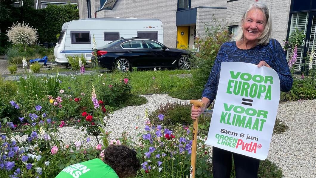 Een inwoner staat met een poster van GroenLinks-PvdA in de hand voor het huis terwijl Alma Feenstra een plantje plant