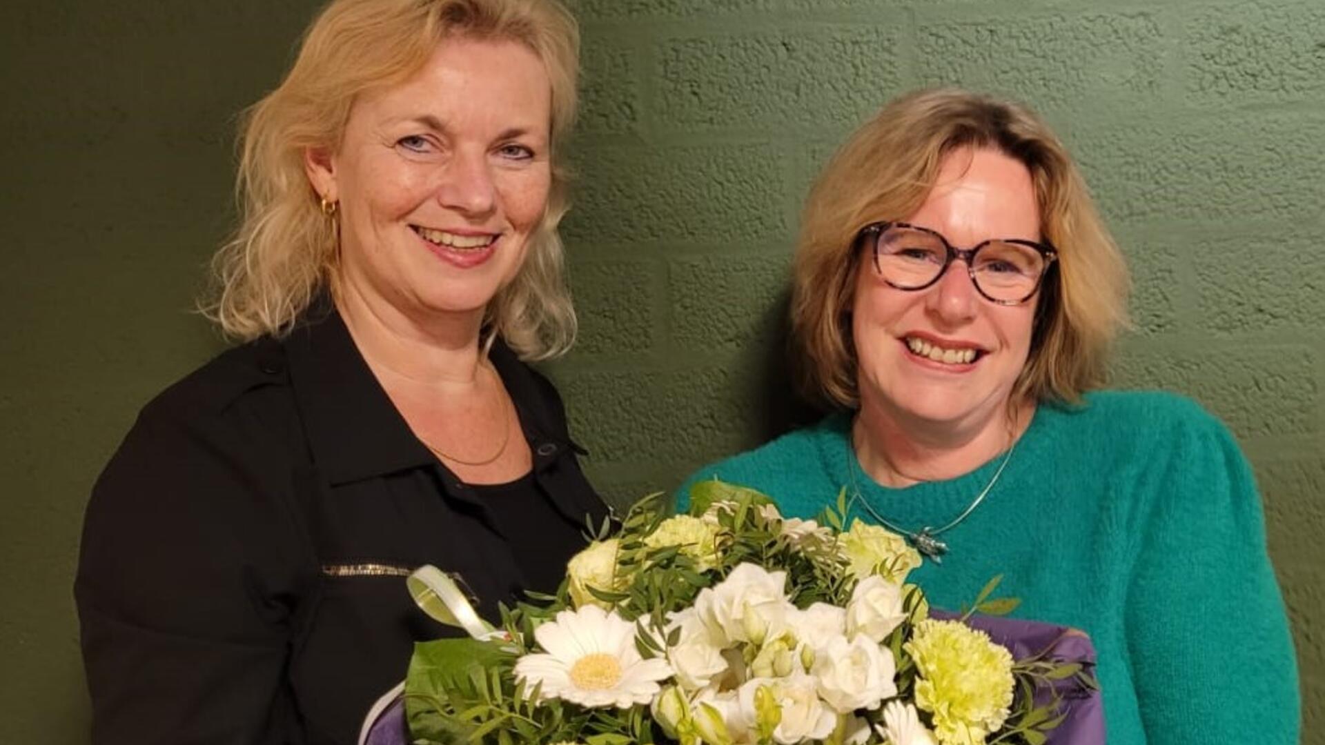 Cora Coster en Boukje Cuelenaere staan met een bos bloemen voor een groene muur
